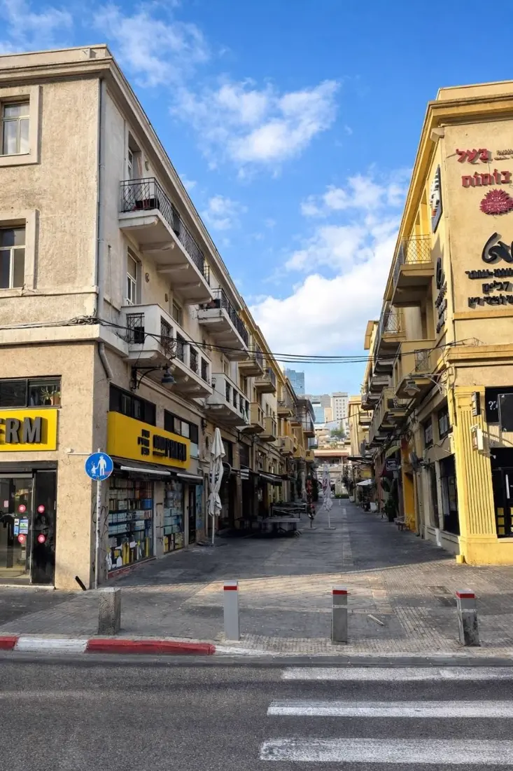 אותו רחוב הבוקר: התריסים מורמים, הרובע מתעורר לאט.